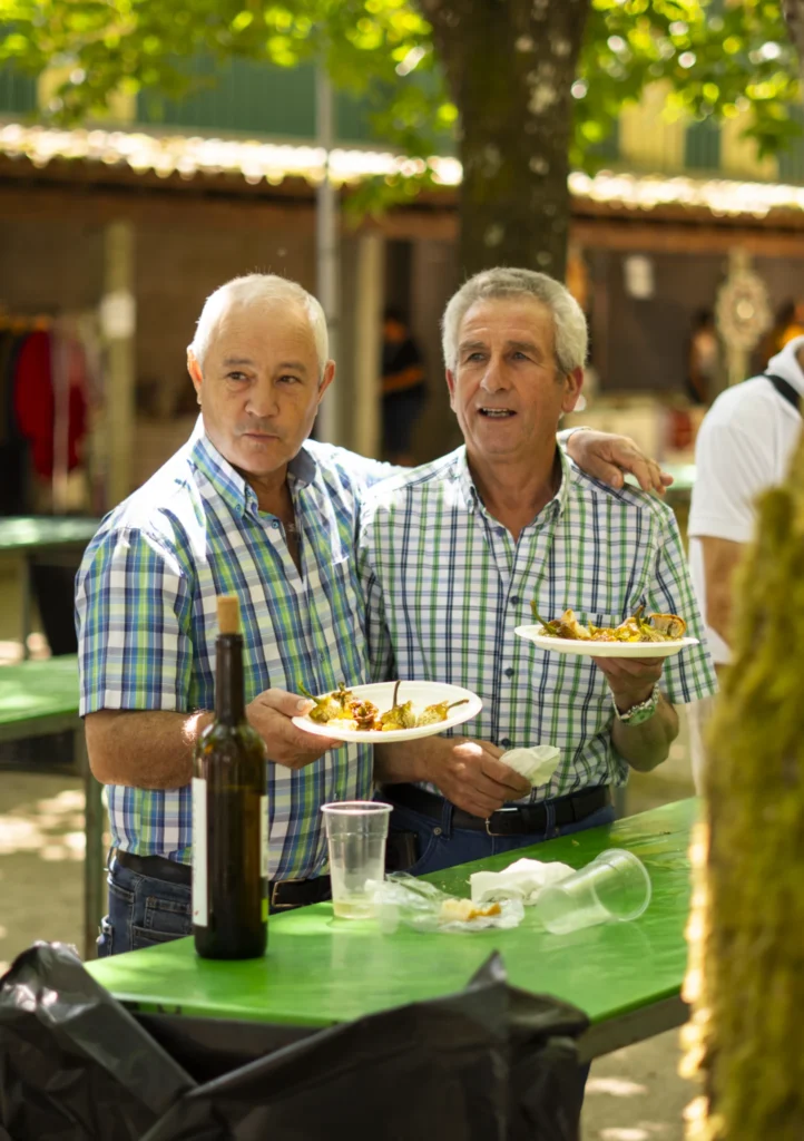 Dous veciños amosan os seus pratos de pementos xunto a unha botella de viño