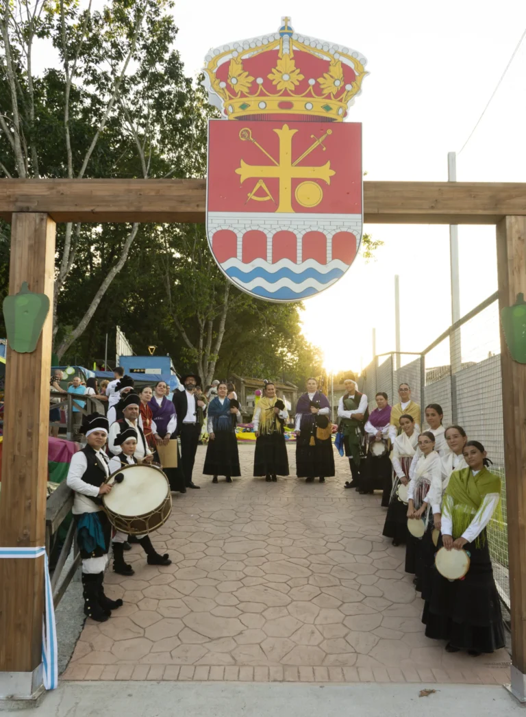 Grupo folclórico agarda baixo o arco de entrada co escudo de A Arnoia ao solpor