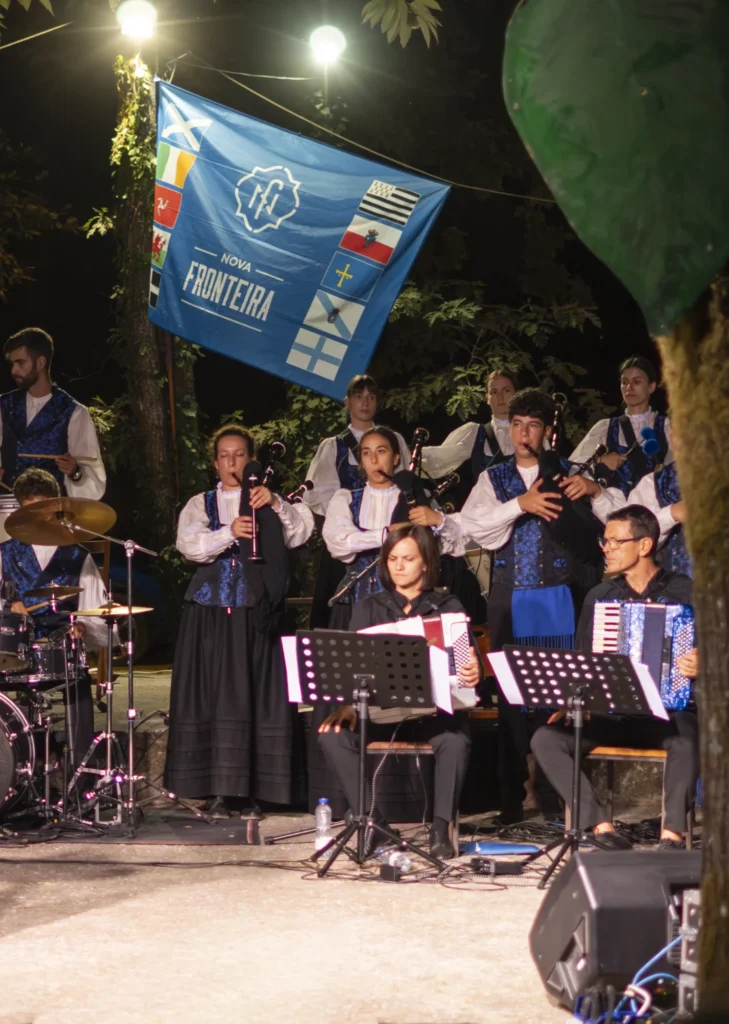 Banda de gaitas e acordeóns actuando de noite baixo unha bandeira con símbolos celtas
