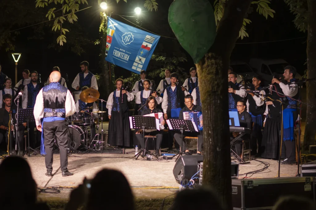 Banda de gaitas e acordeóns actuando de noite no escenario, dirixida polo seu director