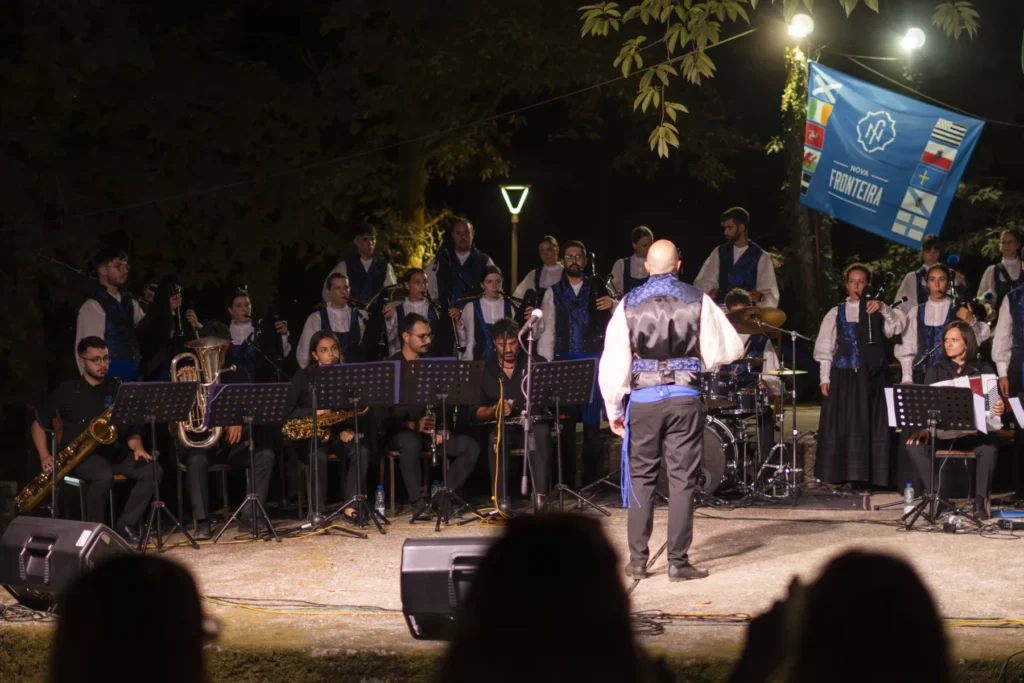 Banda de música tradicional actúa de noite con gaitas, vento e percusión dirixida polo director
