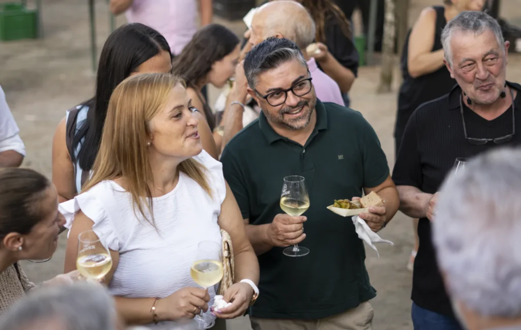 Asistentes brindan con viño branco e comparten unha ración de pementos na carballeira da Arnoia