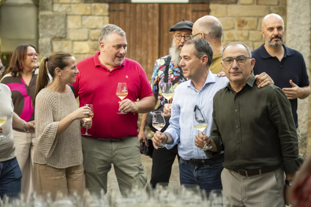Grupo de amigos brindando con copas de viño do Ribeiro diante dun muro de pedra