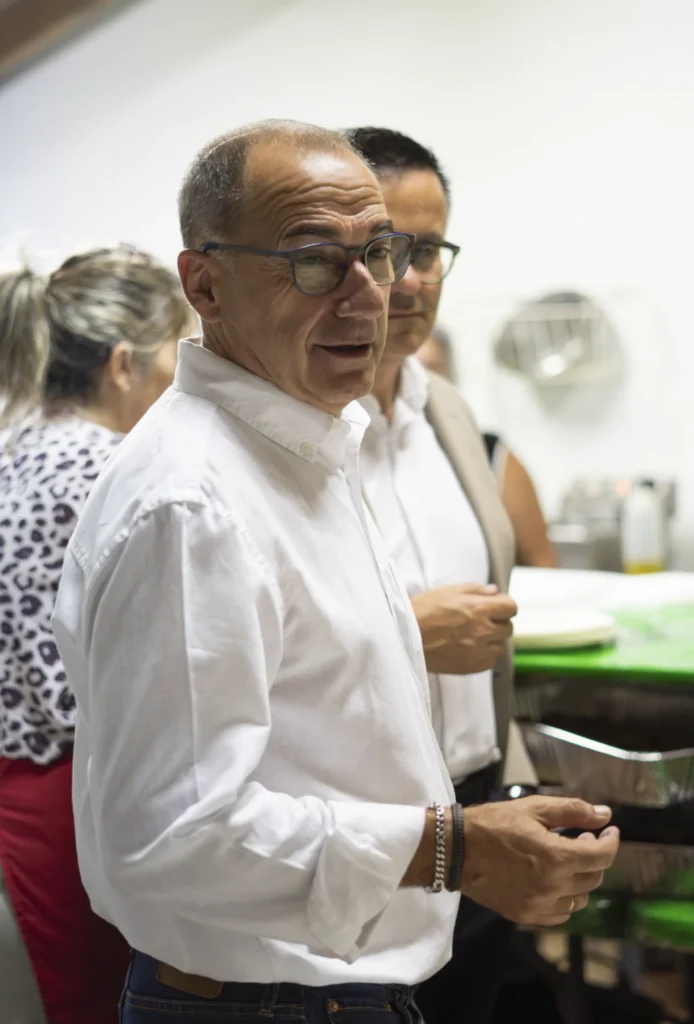 Home de camisa branca conversando na zona de servizo, con bandexas de pementos ao lado