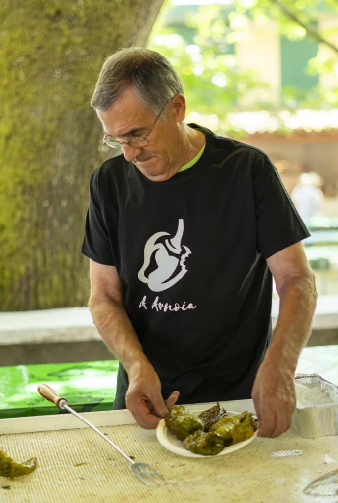 Home cunha camiseta do pemento da Arnoia servindo un prato de pementos fritidos