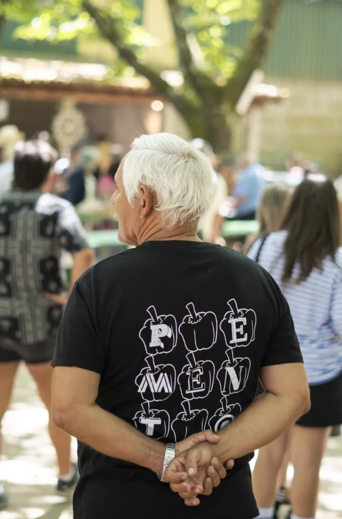 Home de costas cunha camiseta na que se le PEMENTO entre a xente da festa