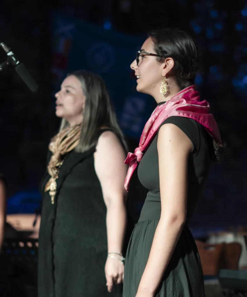 Dúas cantantes de perfil sobre o escenario nocturno durante a actuación musical da festa