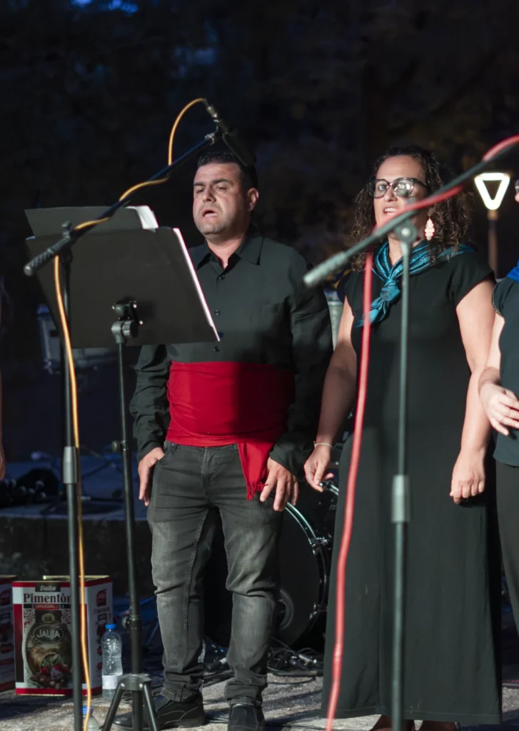 Home con faixa vermella e muller cun pano azul cantando diante dos atrís pola noite