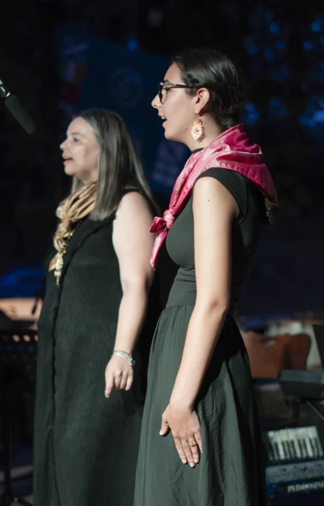 Dúas cantareiras actúan no escenario nocturno, unha delas cun mantón rosa ao pescozo