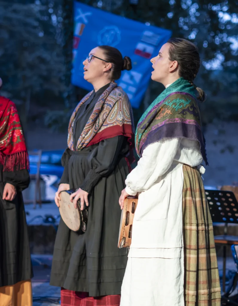 Dúas cantareiras con mantóns tradicionais cantando no escenario, unha delas con pandeireta