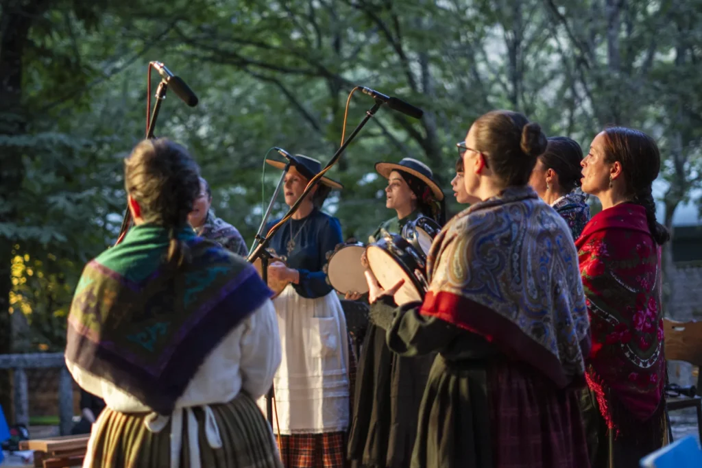 Grupo de cantareiras con mantóns e pandeiretas cantando baixo as árbores ao solpor