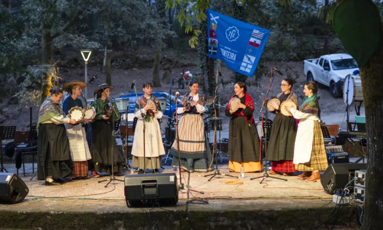 Grupo de cantareiras con traxe tradicional galego toca as pandeiretas no escenario ao solpor