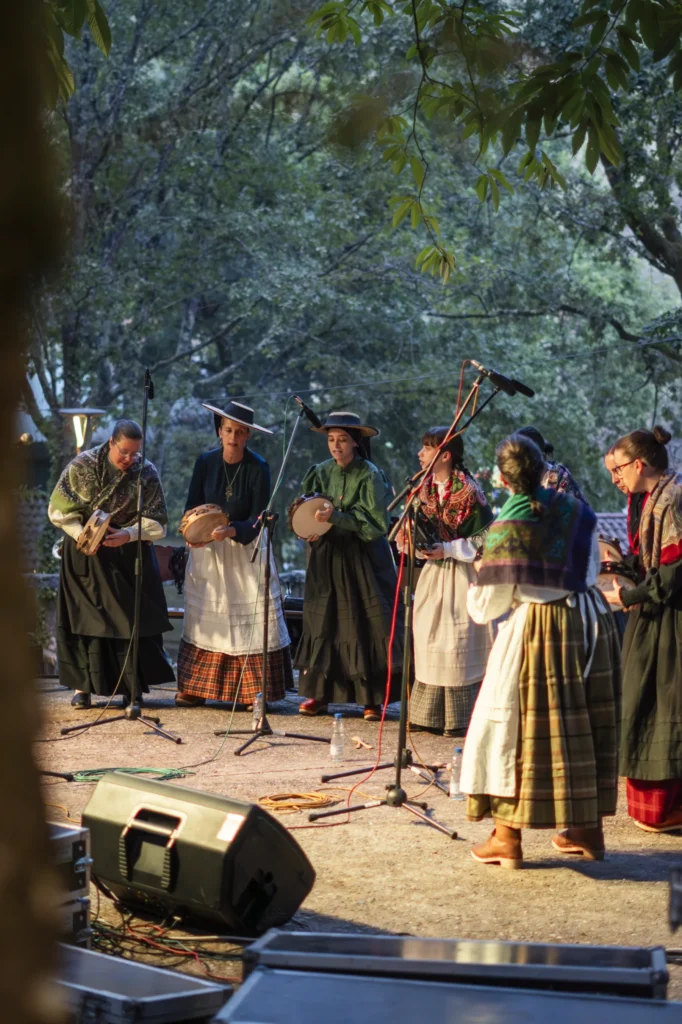 Cantareiras con traxe tradicional galego tocan pandeiretas na carballeira coa luz do serán