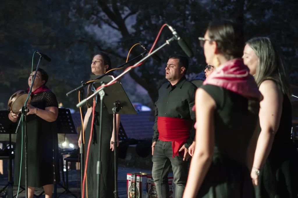 Cantareiras e un cantareiro con faixa vermella interpretan música tradicional no escenario nocturno