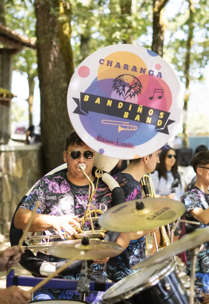 Músico da charanga tocando o bombardino xunto á batería entre as árbores do recinto