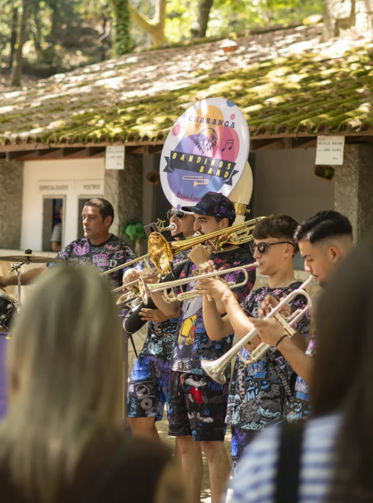Metais da charanga tocando trombón e trompetas diante do posto de comidas do recinto