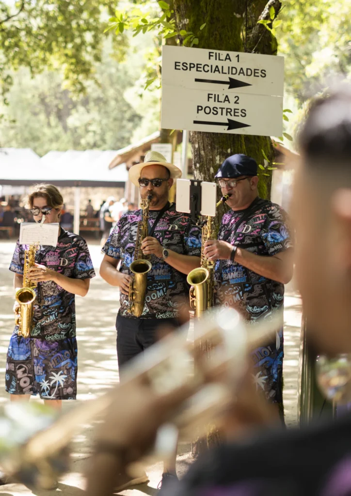 Tres saxofonistas dunha charanga tocando baixo o cartel das filas de degustación