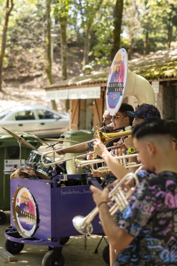 Músicos da charanga tocan trompetas e sousafón xunto ao carro de percusión no recinto