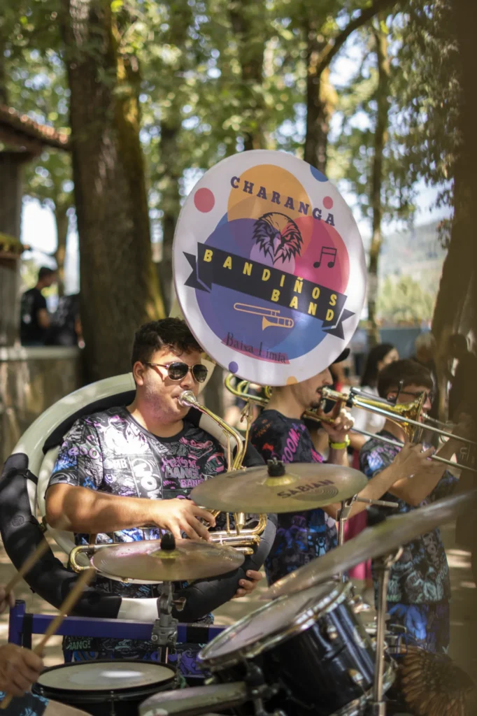 Músicos dunha charanga con tuba, trombóns e bombo animando o recinto arborado da festa