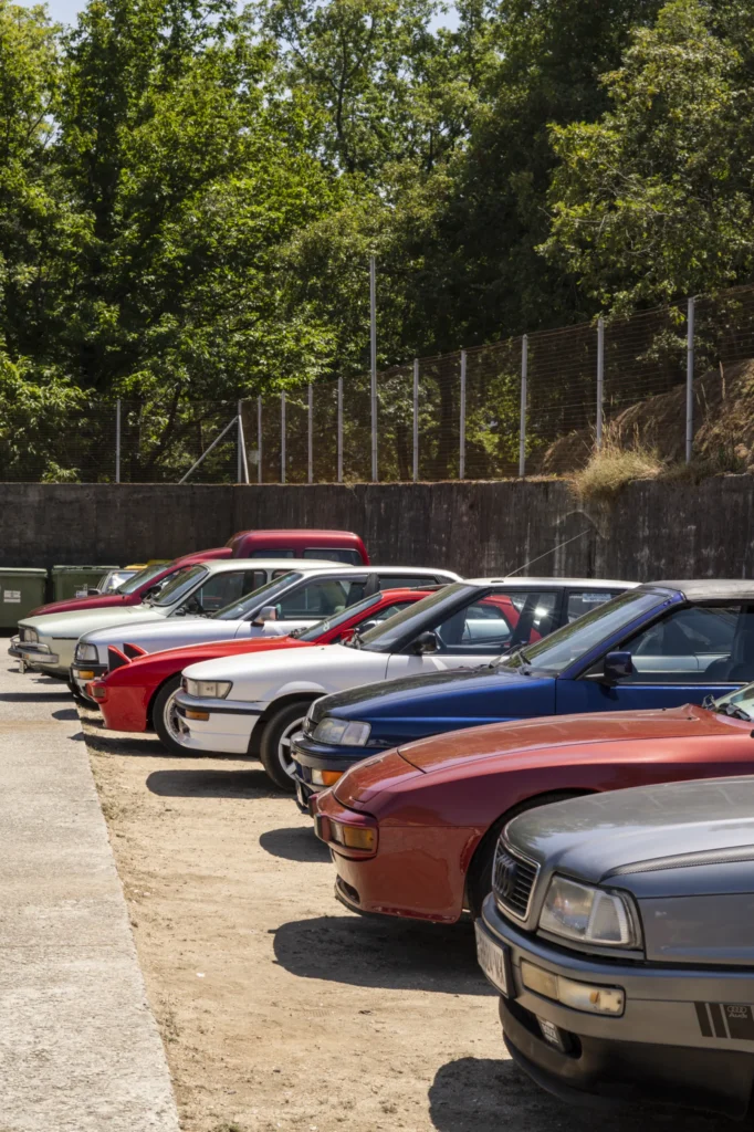 Coches clásicos aparcados en fila baixo o sol nunha explanada durante a xornada festiva