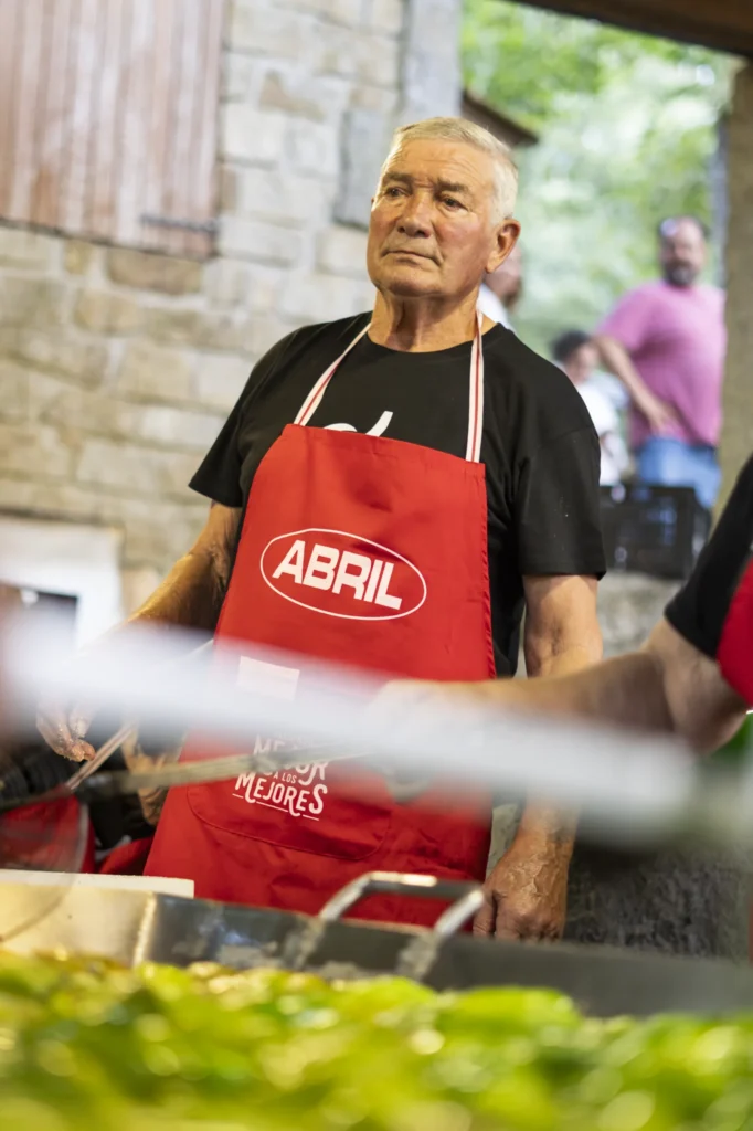 Cociñeiro con mandil vermello xunto á grella onde se asan os pementos da Arnoia