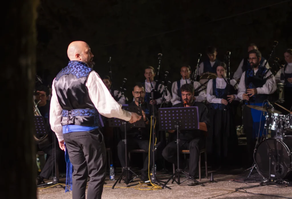 Director dirixe a banda de gaitas con chalecos azuis durante o concerto nocturno da festa