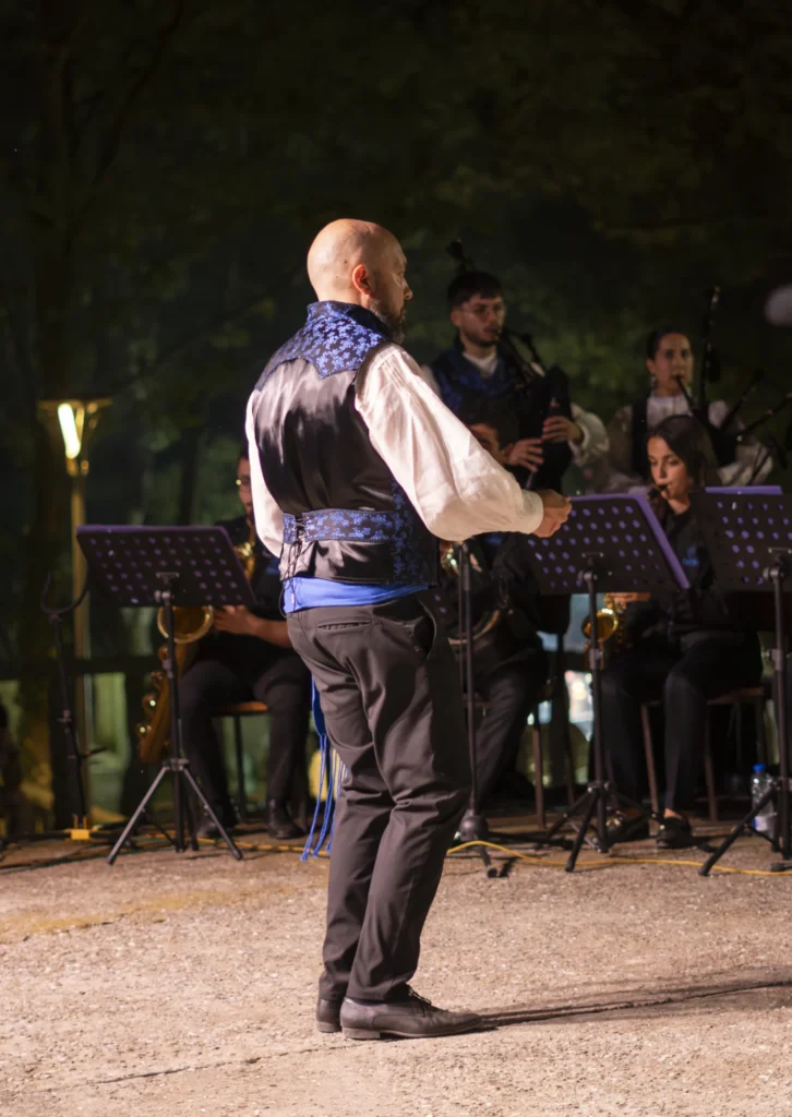Director con chaleco tradicional dirixindo a banda de gaitas na actuación nocturna