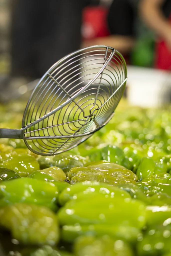 Escumadeira metálica sobre unha montaña de pementos da Arnoia fritidos e brillantes en aceite