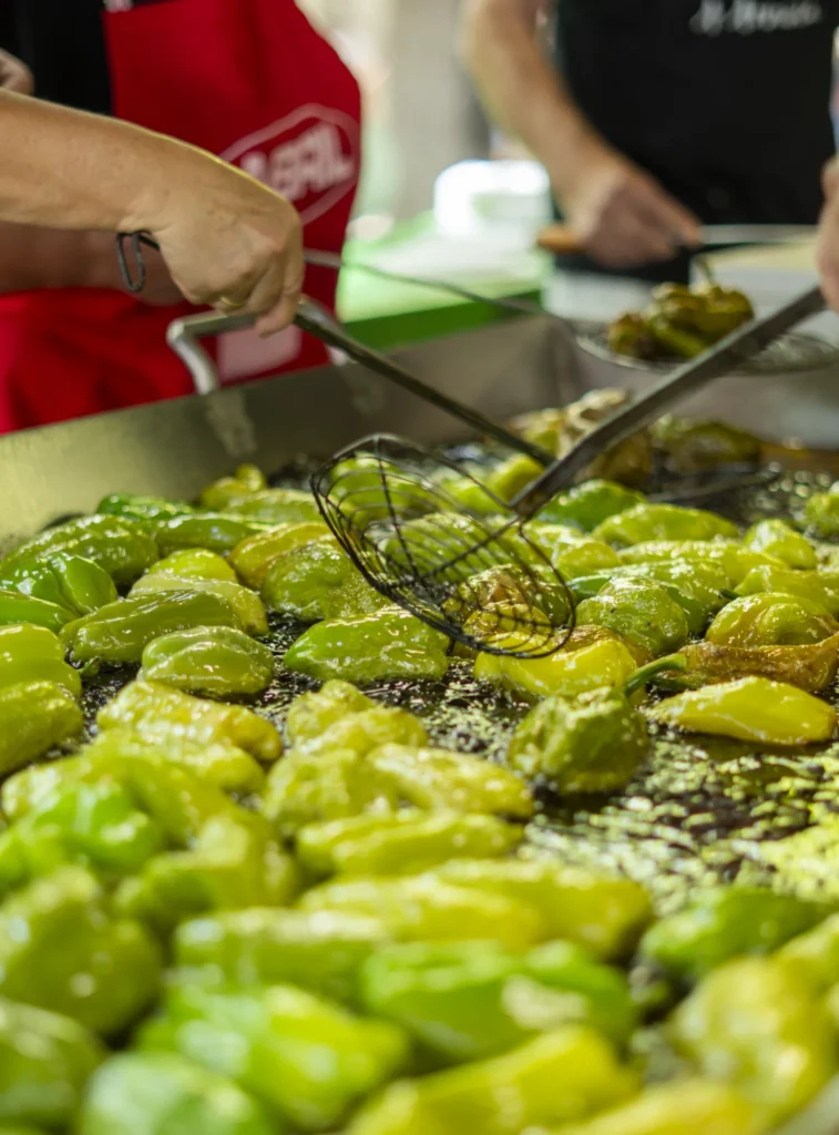 Mans con espumadeira remexen centos de pementos fritindo na gran chapa do posto de degustación