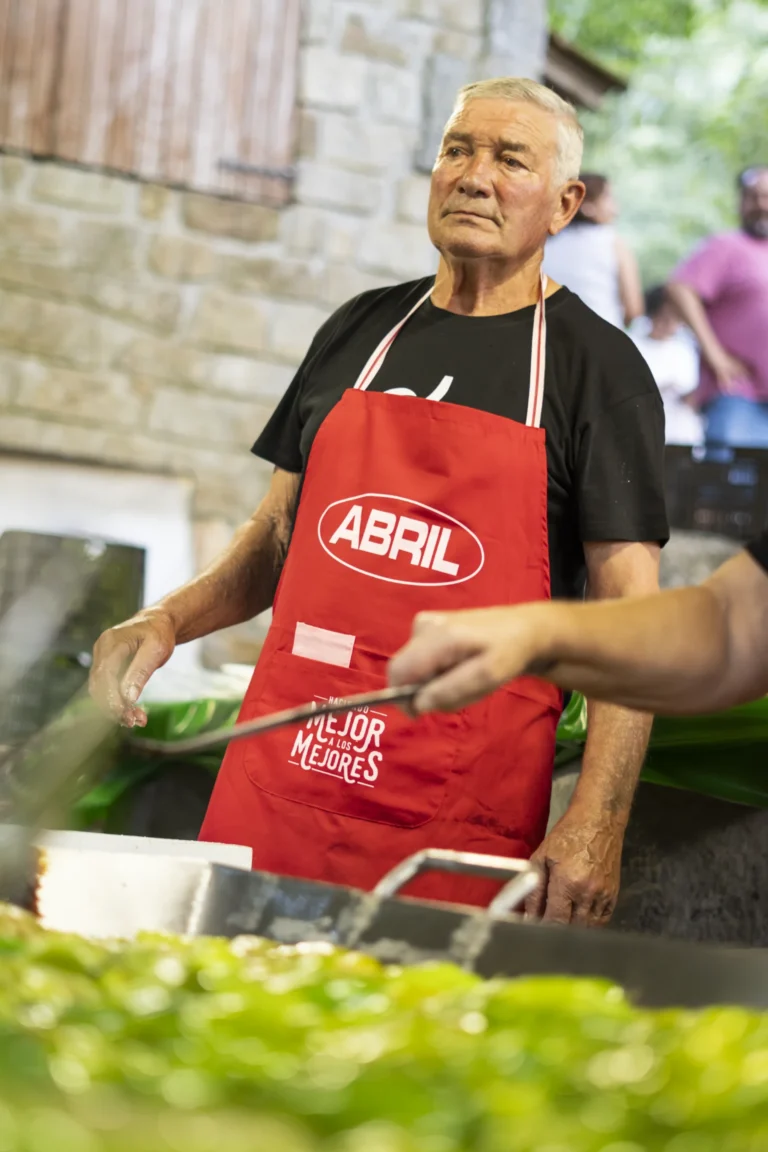 Cociñeiro con mandil vermello frite pementos da Arnoia sobre a grella durante a festa