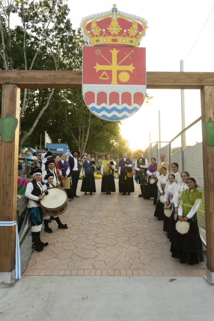 Grupo folclórico con gaitas e pandeiretas agarda baixo o arco de entrada da Festa do Pemento
