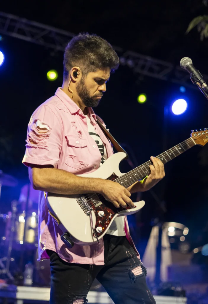 Guitarrista con camisa rosa tocando unha guitarra eléctrica branca no concerto nocturno da festa