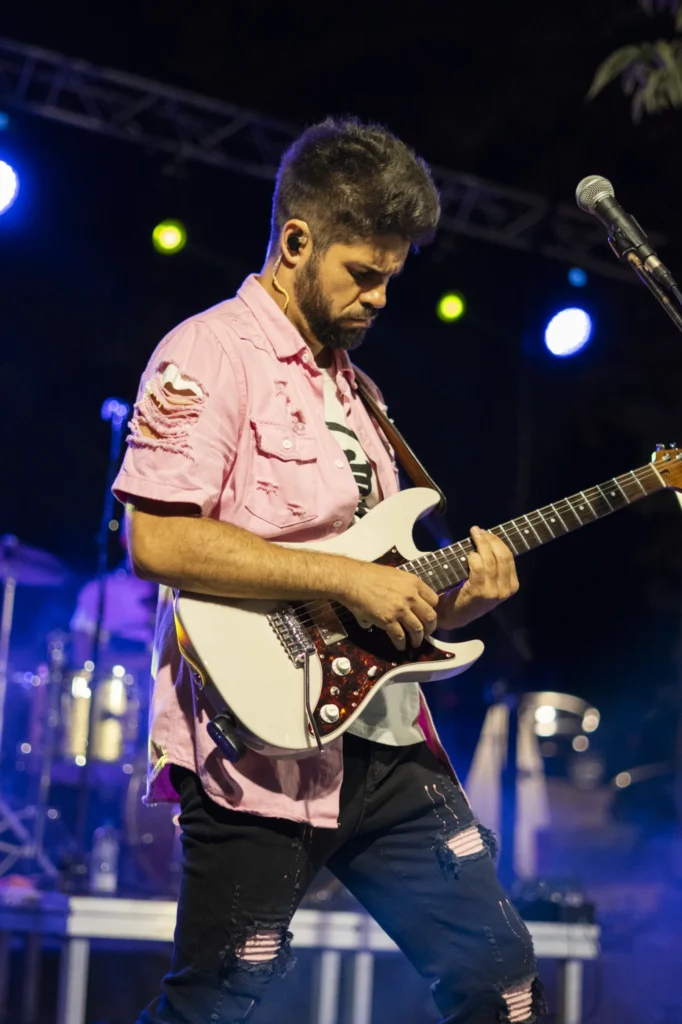 Guitarrista con camisa rosa toca a guitarra eléctrica baixo as luces do escenario nocturno