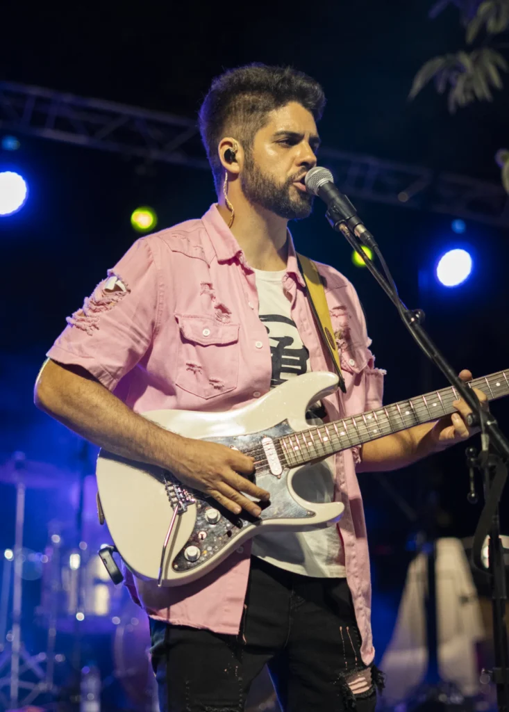 Guitarrista con camisa rosa cantando ante o micrófono no concerto nocturno da festa