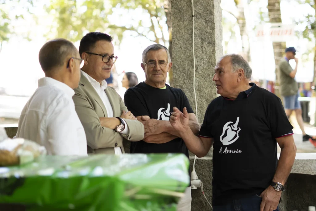 Catro homes conversan na carballeira, dous deles coa camiseta do pemento da Arnoia
