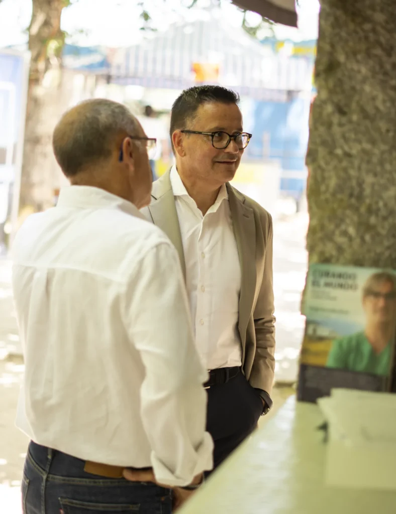 Dous homes conversan á sombra das árbores no recinto da Festa do Pemento