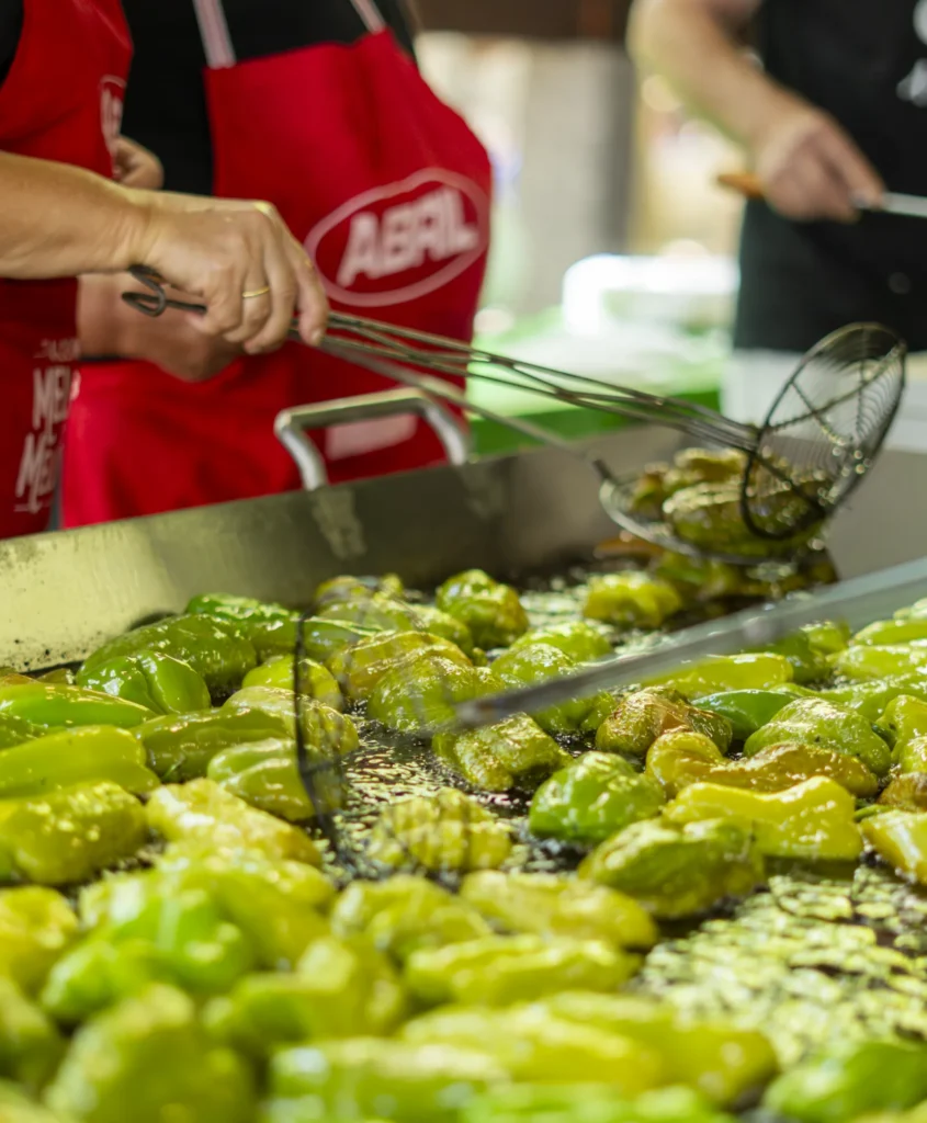 Mans cun mandil vermello remexendo os pementos que se fritan na chapa da festa