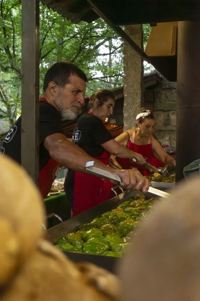 Cociñeiros con mandil vermello serven pementos fritos nunha bandexa baixo a carpa do recinto