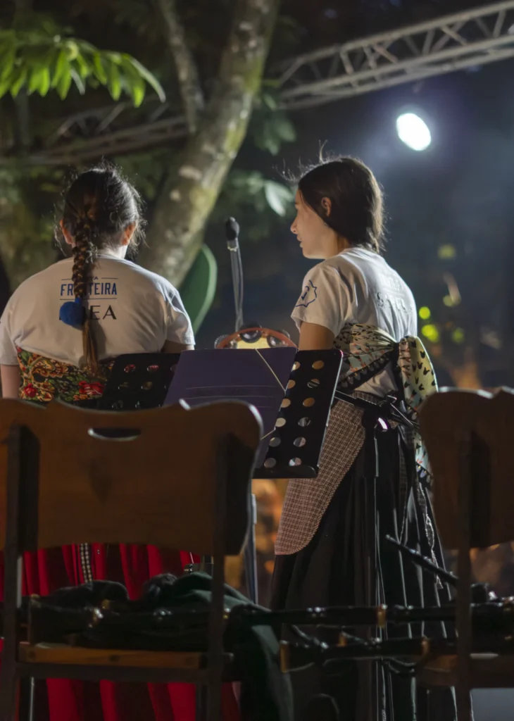 Dúas mozas do grupo tradicional, de costas no escenario nocturno, con saias e pandeireta