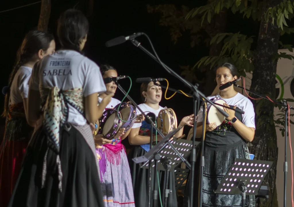 Mozas tocando a pandeireta e cantando no escenario nocturno da Festa do Pemento