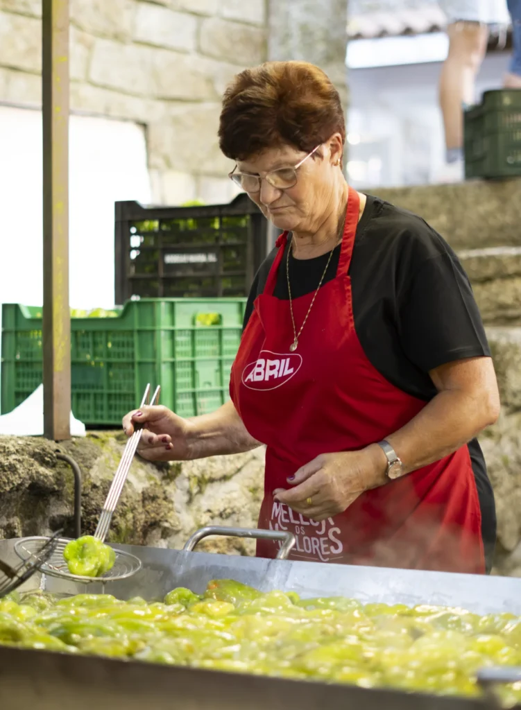 Muller con mandil vermello fritindo pementos de Arnoia nunha gran tixola do recinto festivo