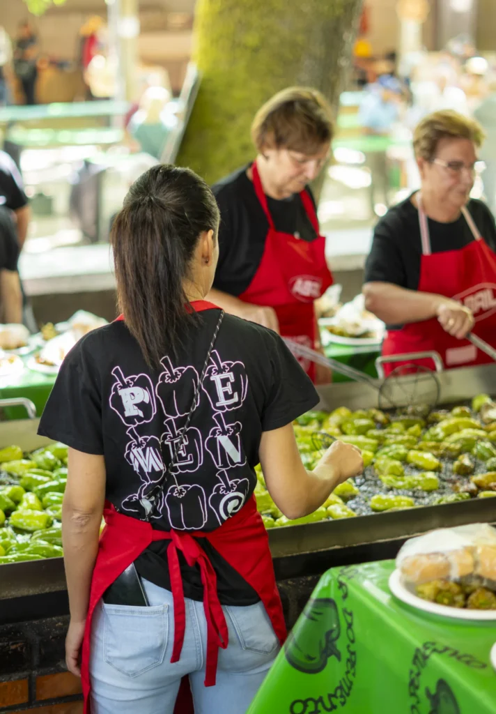 Cociñeiras con mandil vermello fritindo pementos nas grandes planchas da degustación popular