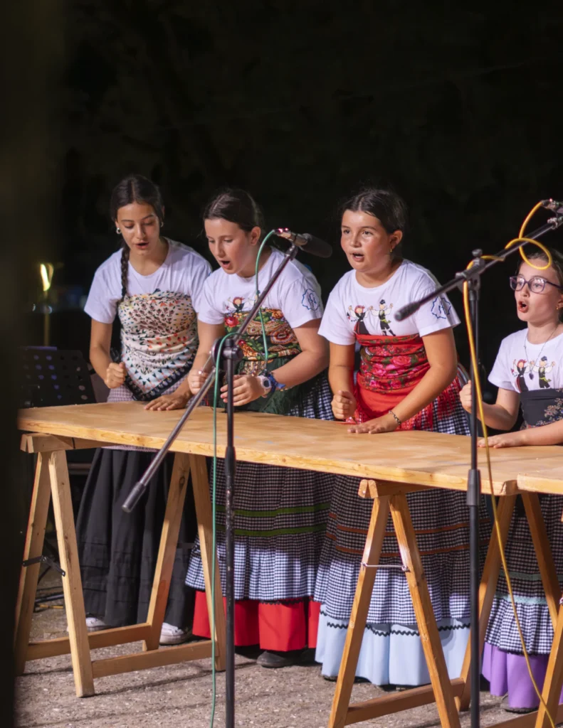 Catro nenas cantan a coro golpeando a mesa de madeira no escenario nocturno da festa