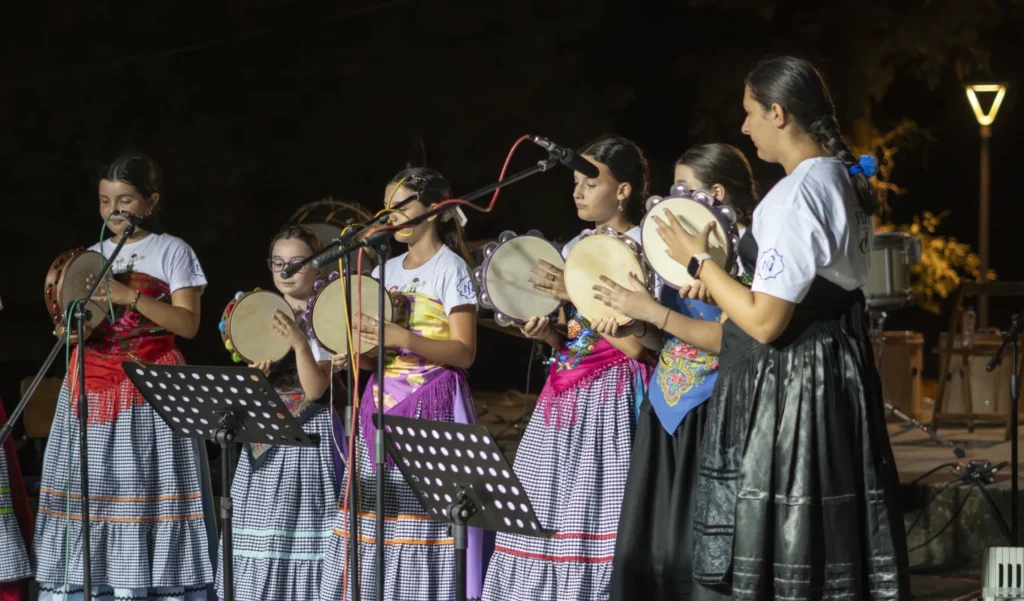 Nenas con saias de cadros e mantóns tocando a pandeireta no escenario nocturno