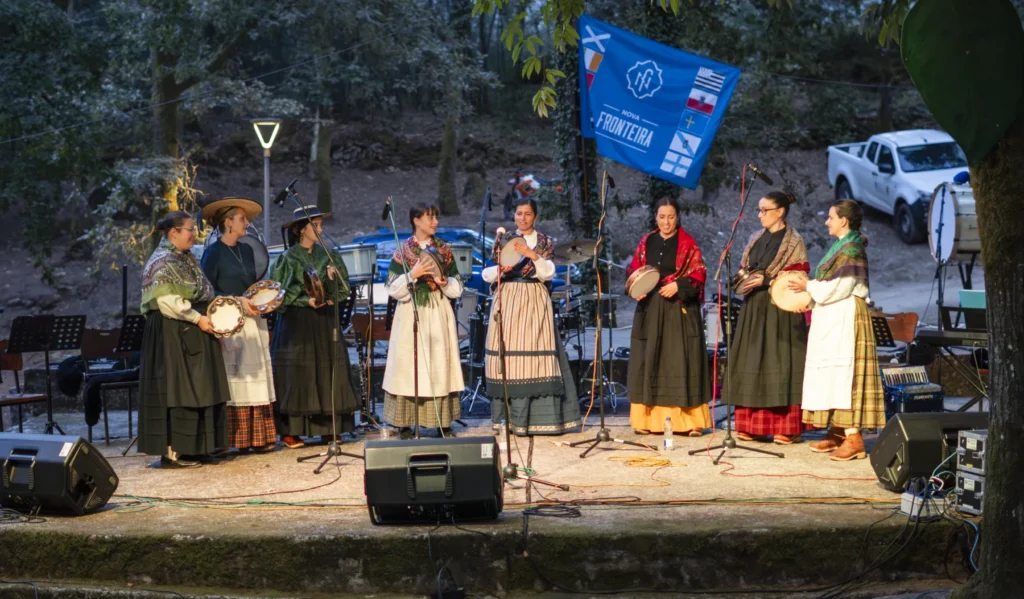 Grupo de pandeireteiras con traxe tradicional canta no escenario da carballeira ao anoitecer