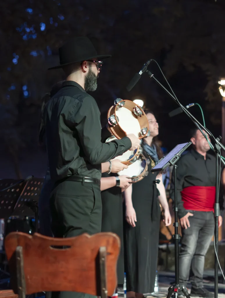 Músico con sombreiro negro toca a pandeireta no escenario nocturno xunto á cantareira