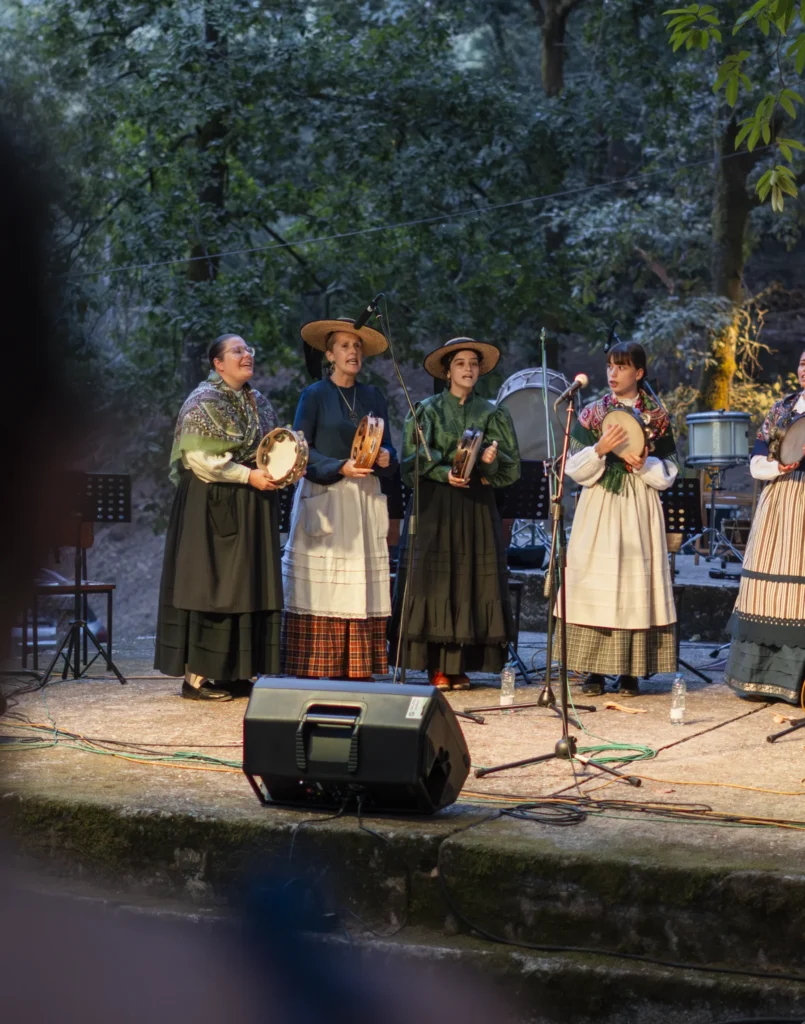 Pandereteiras con traxe tradicional cantando no escenario ao solpor rodeadas de arboredo