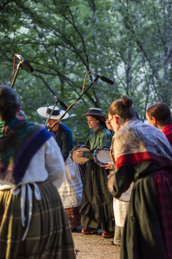 Mulleres con traxe tradicional galego tocan a pandeireta ante os micrófonos, entre a arboreda