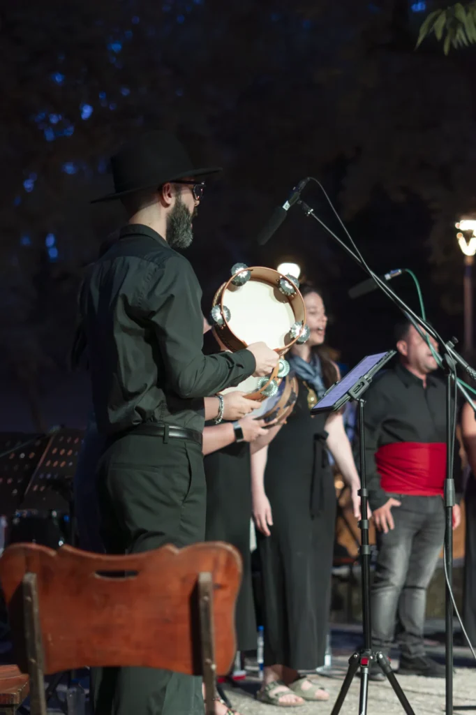 Percusionista con sombreiro negro tocando a pandeireta xunto ás cantareiras no escenario nocturno