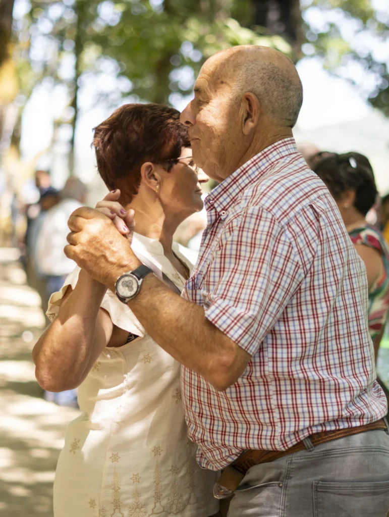 Parella maior baila agarrada baixo as árbores durante a verbena da festa